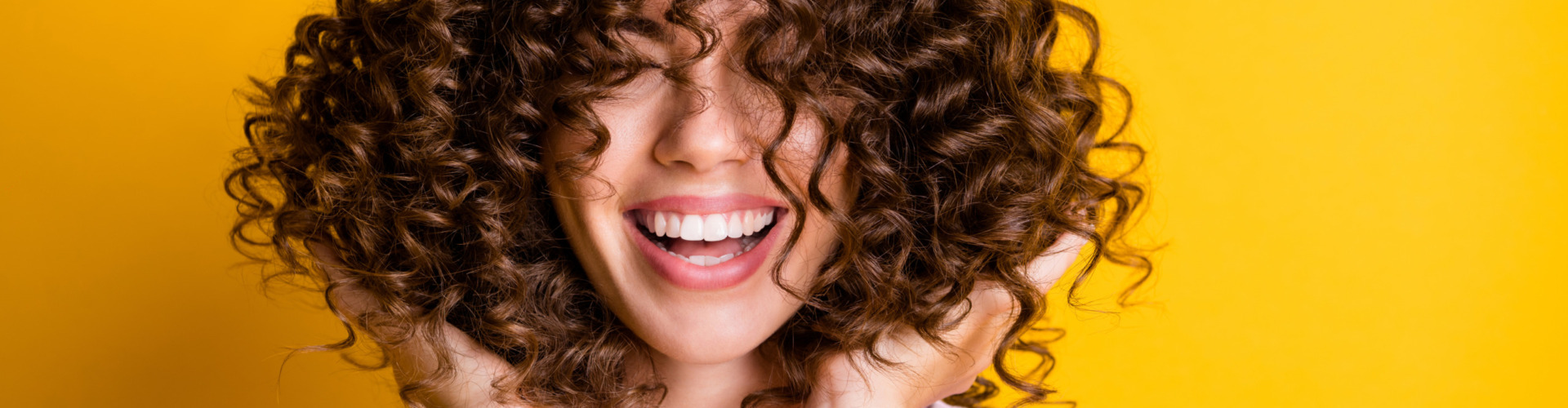 Photo portrait of girl with curly hairstyle wearing t-shirt laughing touching hair isolated on bright yellow color background.